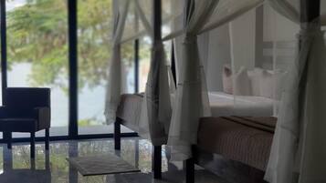 Ein Schlafzimmer mit Bett, Stuhl und Meerblick durch große Fenster.