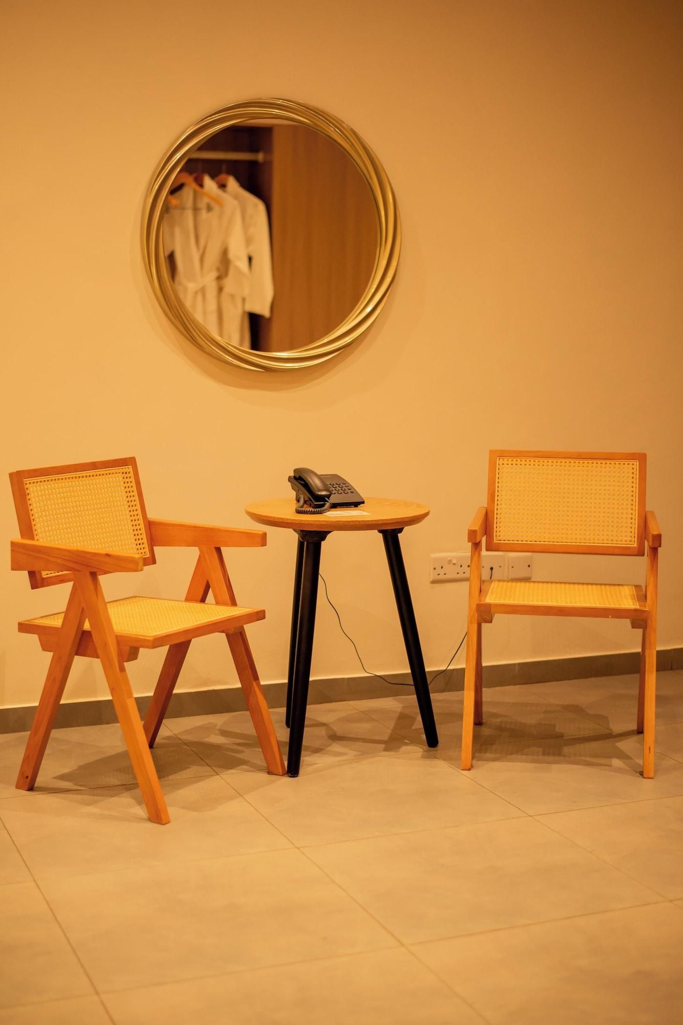 A room with two wooden chairs with woven seats, a small round table with a telephone, and a round mirror on the wall.