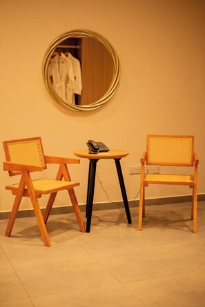 A room with two wooden chairs with woven seats, a small round table with a telephone, and a round mirror on the wall. - Waters Edge By Serendib (Liwonde)