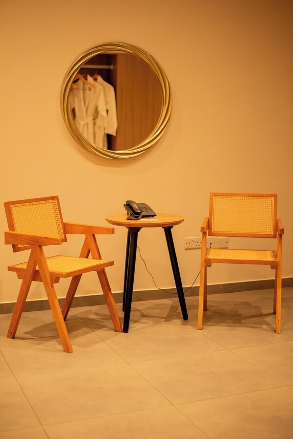 A room with two wooden chairs with woven seats, a small round table with a telephone, and a round mirror on the wall. - Waters Edge By Serendib (Liwonde)