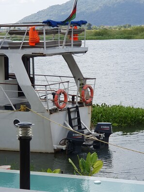 A boat docked at a calm water body with a ladder leading to the deck, a Yamaha outboard motor, and life rings on the side. - Waters Edge By Serendib (Liwonde)