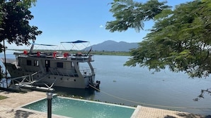 A boat docked by a calm lake with a small pool and lounge chairs. - Waters Edge By Serendib (Liwonde)
