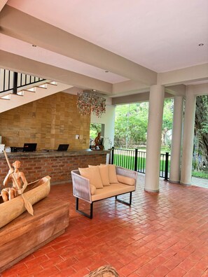 A spacious indoor area with a wooden bench, a cushioned sofa, and a stone wall. - Waters Edge By Serendib (Liwonde)