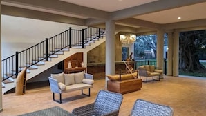 A spacious living area with a staircase, wicker furniture, and a fireplace. - Waters Edge By Serendib (Liwonde)