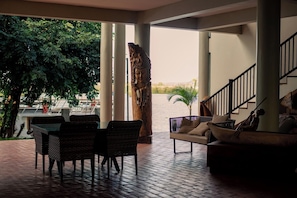 An indoor area with a brick floor, a sofa, a dining table with chairs, and a staircase. - Waters Edge By Serendib (Liwonde)