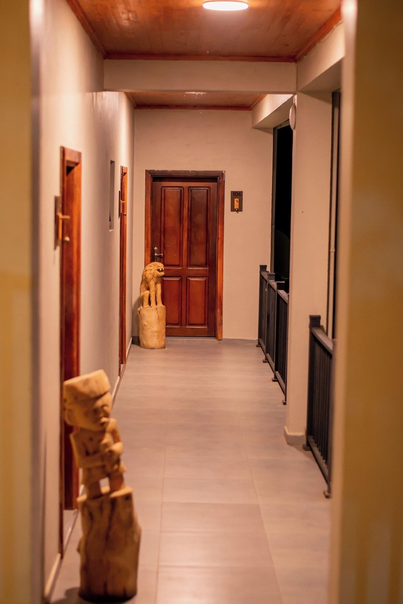 Un pasillo con una puerta de madera, una placa con un número y una estatua.