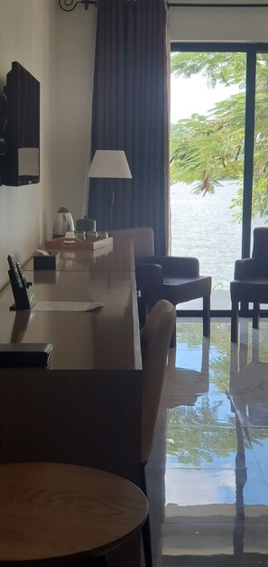 Une chambre d’hôtel équipée d’une table à manger, de chaises, d’une lampe, d’une petite table avec un plateau, et offrant une vue sur un plan d’eau grâce à de grandes fenêtres.