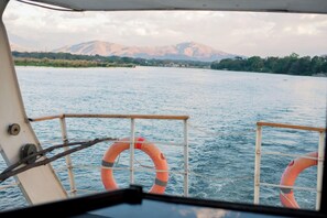 A boat with lifebuoys on deck, a view of a calm river, and distant mountains. - Waters Edge By Serendib (Liwonde)