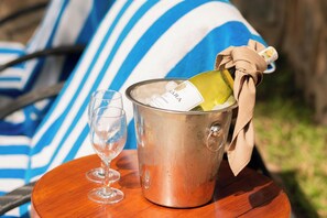 Ein Metallkübel mit einer Champagnerflasche, einem Glas und einem gestreiften Handtuch auf einer Holztischplatte.