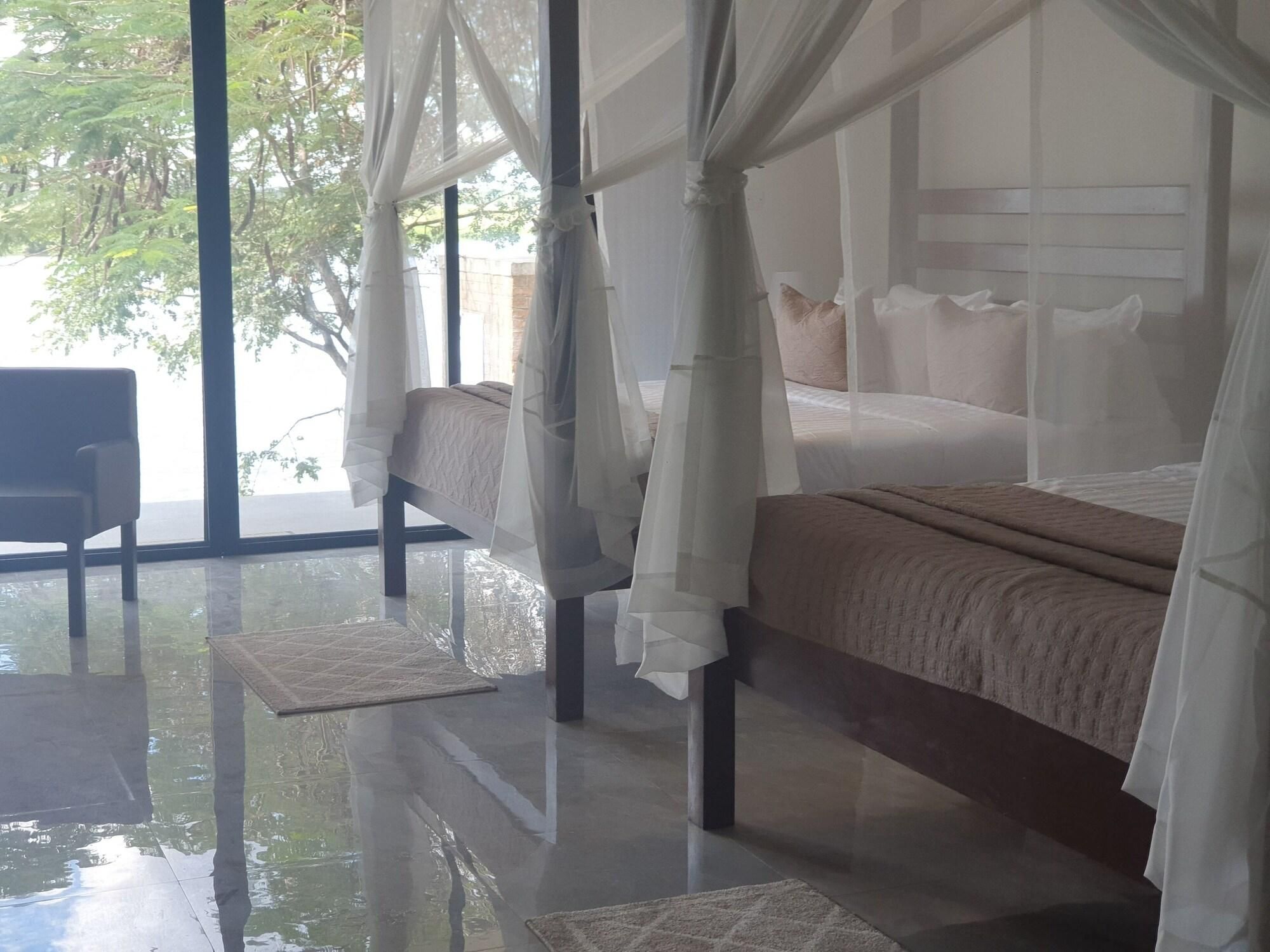 Una camera da letto con un letto a baldacchino, una poltrona e vista su alberi attraverso ampie finestre.