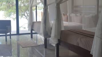 Una camera da letto con un letto a baldacchino, una poltrona e vista su alberi attraverso ampie finestre.