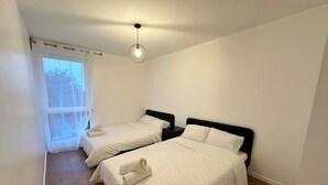 Una camera da letto con due letti, una finestra con tende leggere e un lampadario.