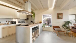 Una cocina moderna con una isla central, taburetes de bar y un comedor con una silla y mesa de madera.