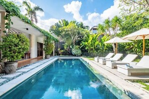 A swimming pool with lounge chairs and umbrellas, surrounded by lush greenery and a clear sky. - Central Seminyak Villa Martini (Bali)