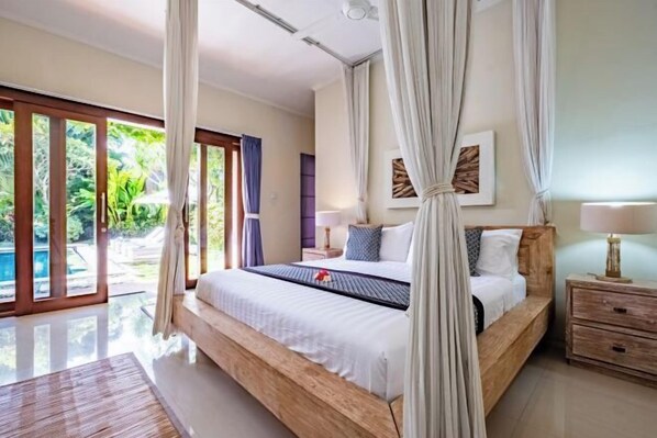A bedroom with a large bed, a nightstand, a lamp, and a view of a swimming pool. - Central Seminyak Villa Martini (Bali)