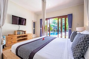 A bedroom with a bed, a TV, a wooden dresser, and a view of a pool. - Central Seminyak Villa Martini (Bali)