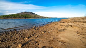 A beach with a rocky shoreline, a forested hill in the background, and a clear blue sky. - “The Sugarloaf Mountain Cabin” A Charming Lakefront Escape!! (Higden)