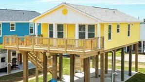 A yellow building with a wooden deck and a blue building in the background. - Brand new beach home 3BR near beach and fishing (Surfside Beach)