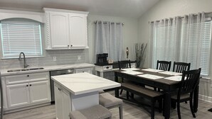 A modern kitchen with white cabinetry, a central island, and a dining area with a dark wooden table and chairs. - Brand new beach home 3BR near beach and fishing (Surfside Beach)