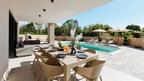 Un espacio de comedor al aire libre con piscina, paredes de piedra y sillones de descanso.