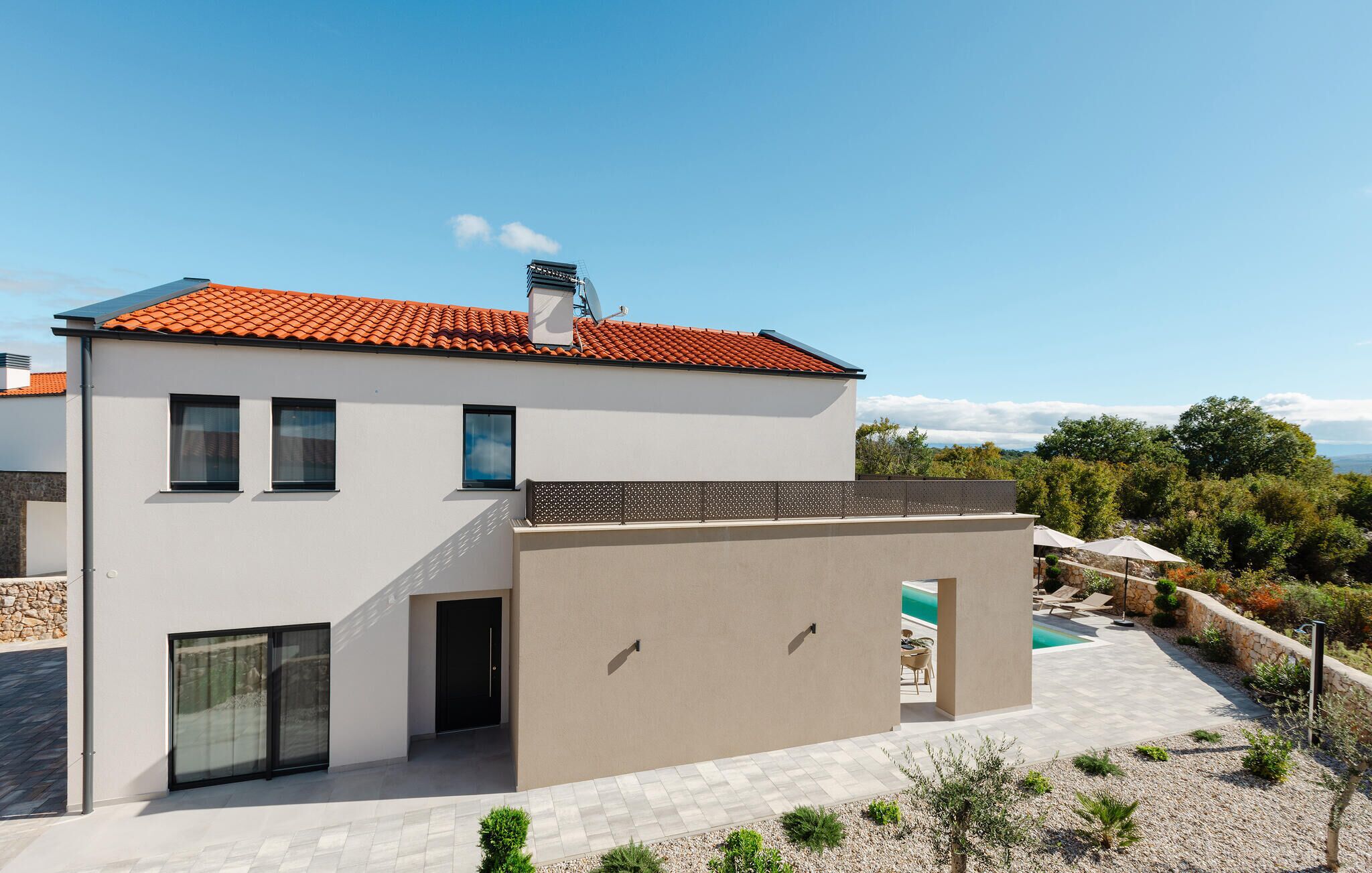 Une maison moderne à deux étages, avec un toit recouvert de tuiles rouges, une piscine et un jardin aménagé.