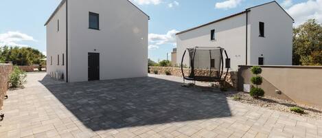 A modern building with a paved courtyard, a swing chair, and a small tree.