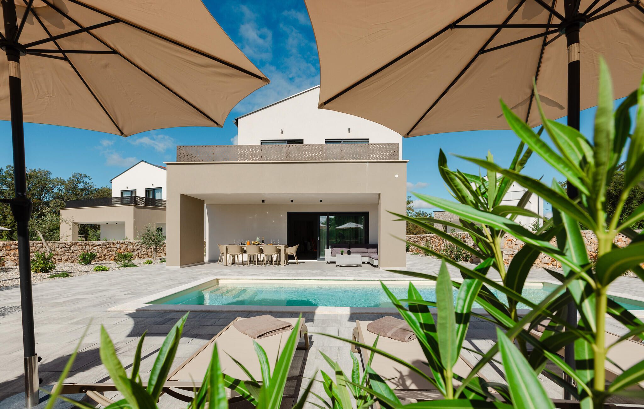 Une maison moderne dotée d’une piscine, d’un espace salon extérieur et de grands parasols.