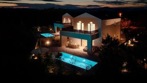 Una casa moderna de dos pisos con piscina, mobiliario exterior y un balcón.