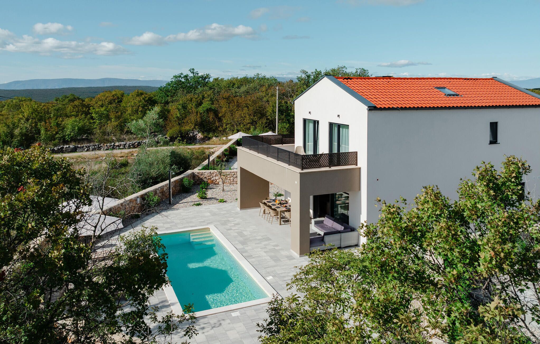 A modern house with a swimming pool, a covered patio, and a view of the surrounding landscape.