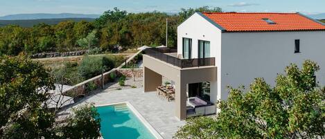 A modern house with a swimming pool, a covered patio, and a view of the surrounding landscape.