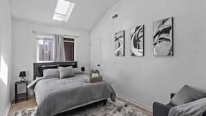Un dormitorio moderno con cama, mesitas de noche, cortinas en la ventana y arte abstracto en la pared.