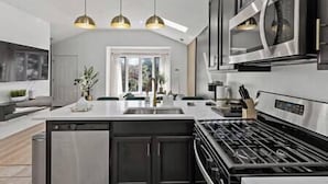 Una cocina moderna con una isla central, electrodomésticos de acero inoxidable, iluminación colgante y vistas al exterior.