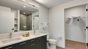 A modern bathroom with a large mirror, two sinks, a toilet, and a shower area.