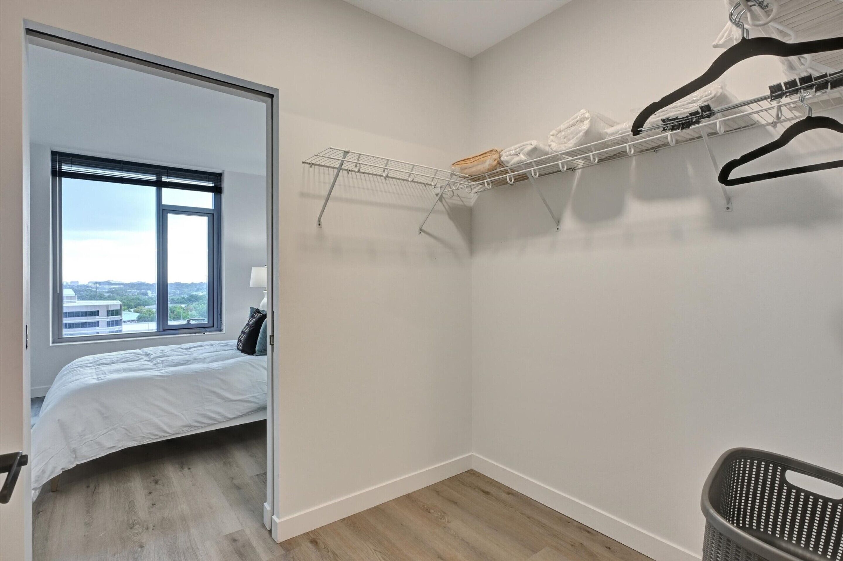 A bedroom with a bed, a window, a metal drying rack, and a laundry basket.
