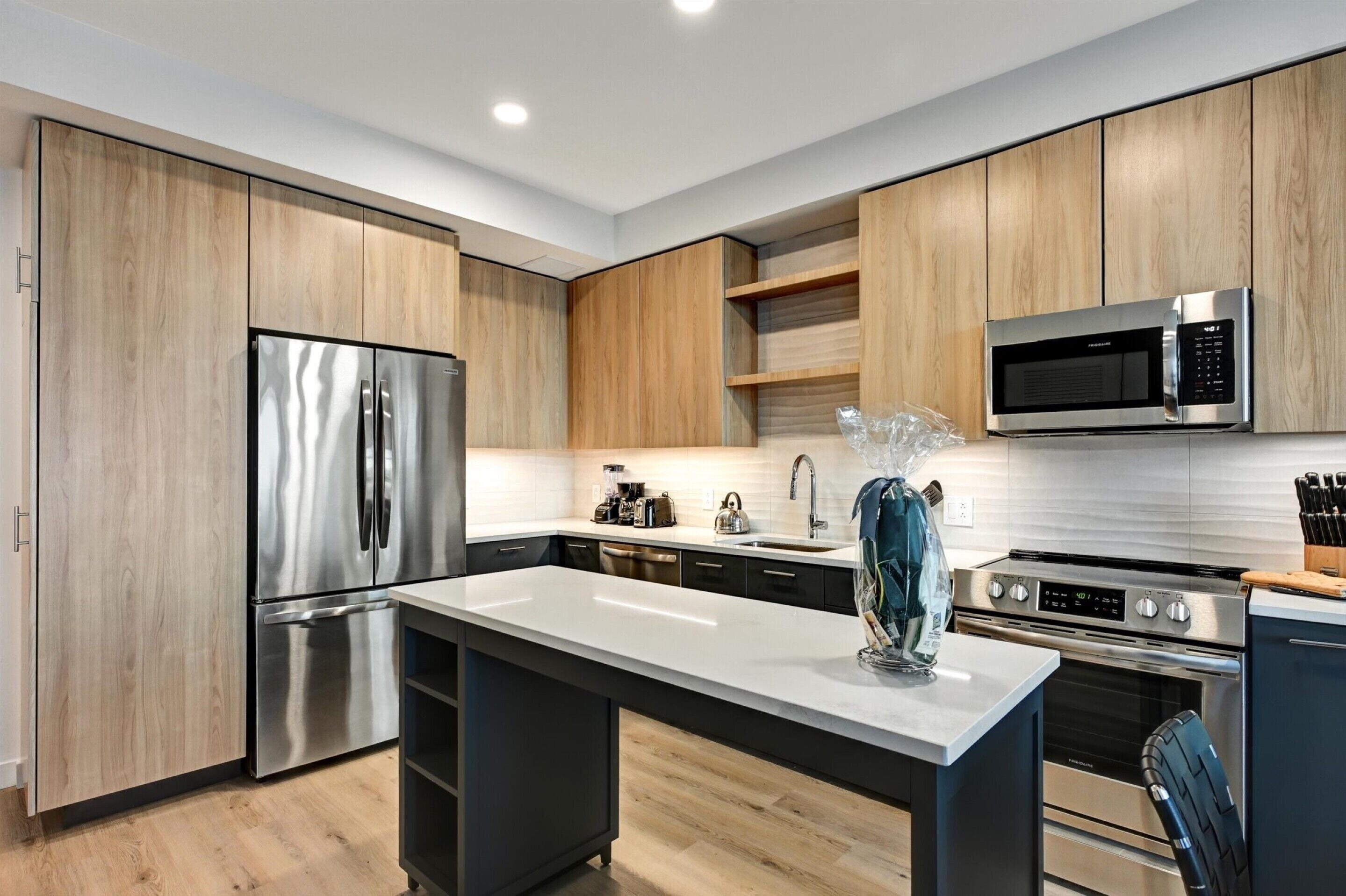 A modern kitchen with wooden cabinets, stainless steel appliances, and a marble countertop.