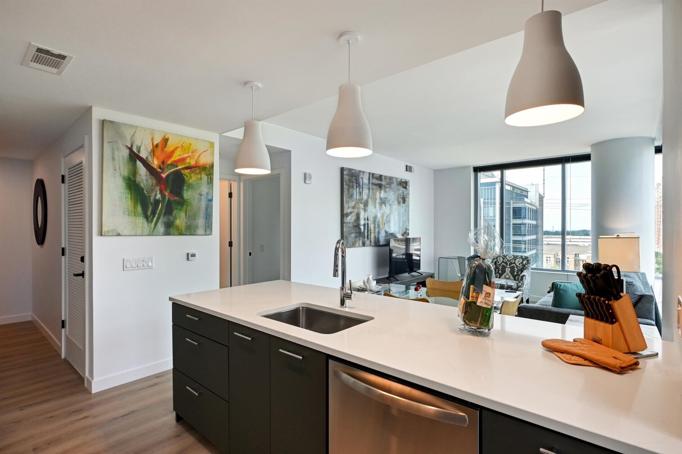 Een moderne keuken met een wit aanrecht, een roestvrijstalen spoelbak en hangende lampen.