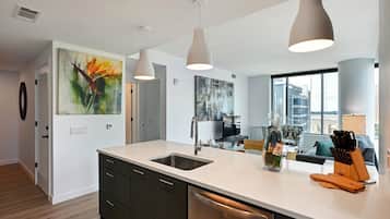 A modern kitchen with a white countertop, stainless steel sink, and overhead pendant lights.