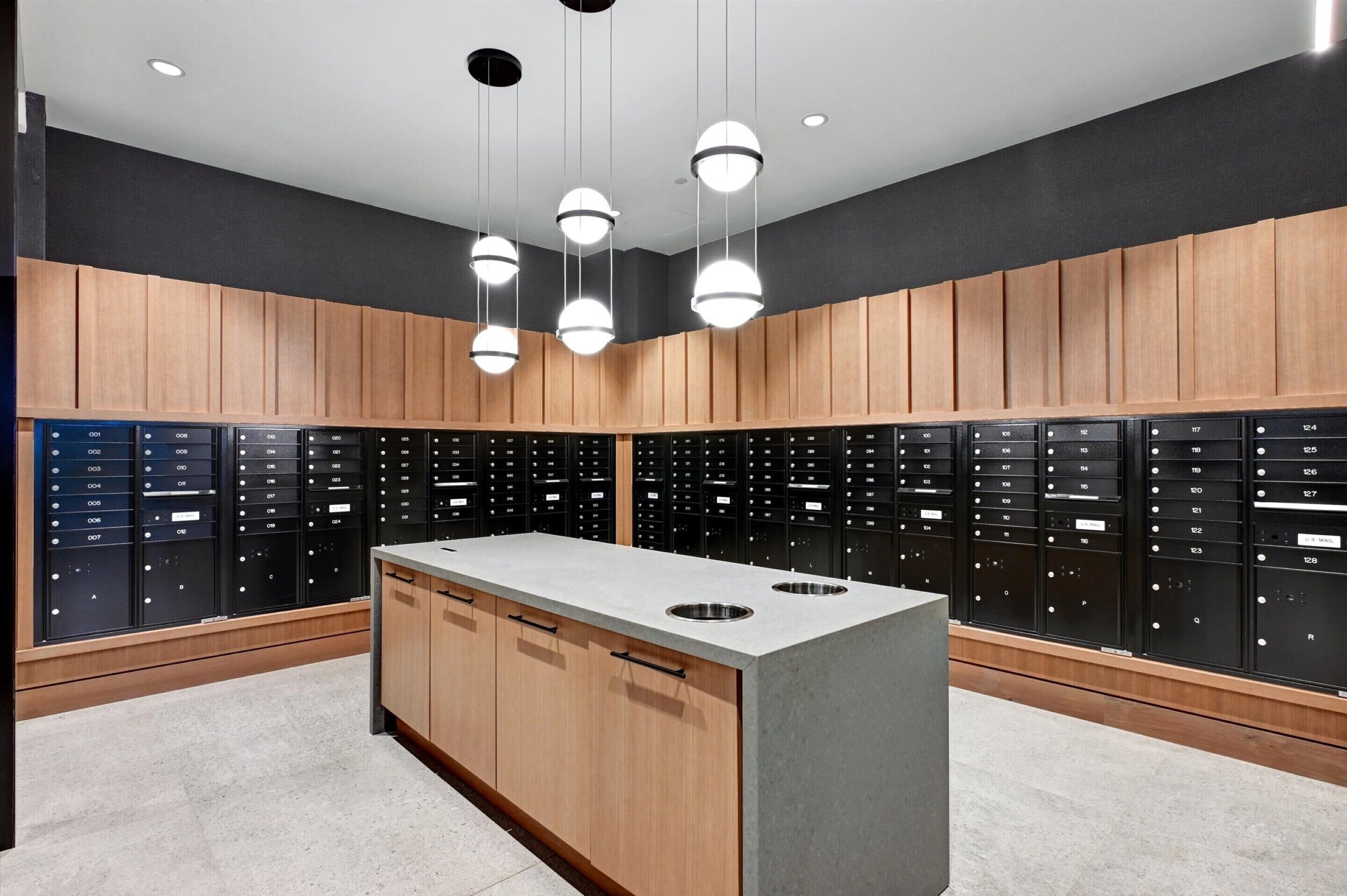 A modern locker room with wooden cabinets and black lockers, featuring a central island with sinks.