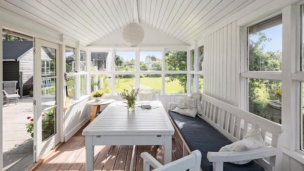 A covered patio with a white table and benches, large windows, and a view of the garden. - 5 bedroom awesome home in Slagelse (Slagelse)
