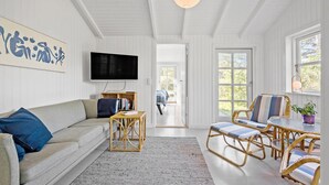 A living room with a sofa, a television, a bookshelf, wicker furniture, and a view through a door. - 5 bedroom awesome home in Slagelse (Slagelse)