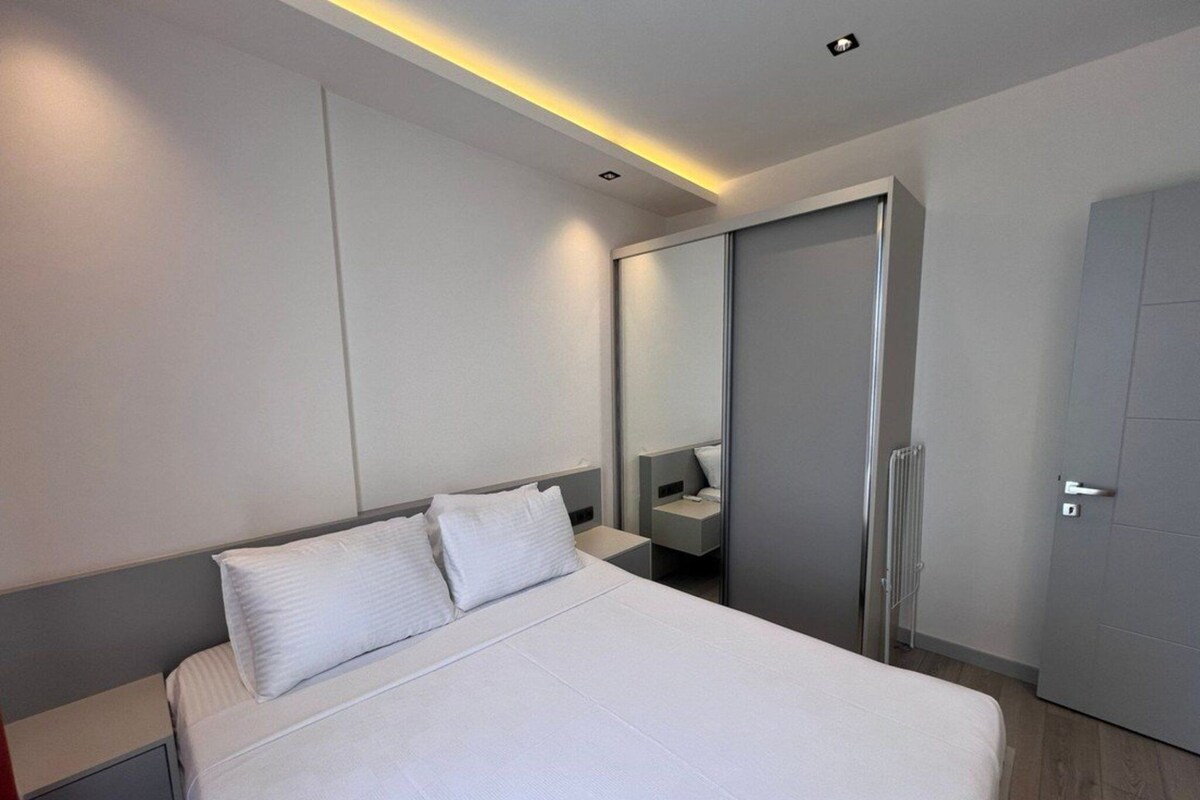 A modern bedroom with a large bed, a bedside table, a mirror, and a wardrobe.