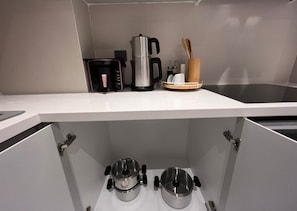 A kitchen with a white countertop, a coffee maker, a kettle, and a wooden utensil holder. There are two stainless steel pots on the lower shelf. - Ulu Residence Alanya (Alanya)