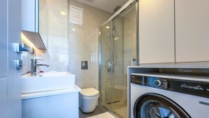 Ein modernes Badezimmer mit Duschkabine aus Glas, einem weißen Waschbecken und einer Waschmaschine mit Frontlader.