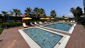 Zona de piscina con dos piscinas, tumbonas y sombrillas amarillas.