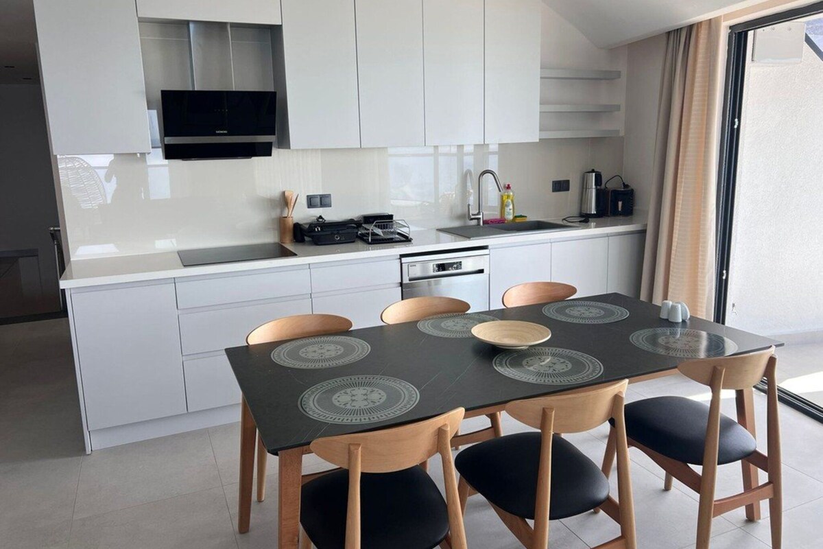 A modern kitchen with white cabinets, a black countertop, and a dining area with a black table and wooden chairs.