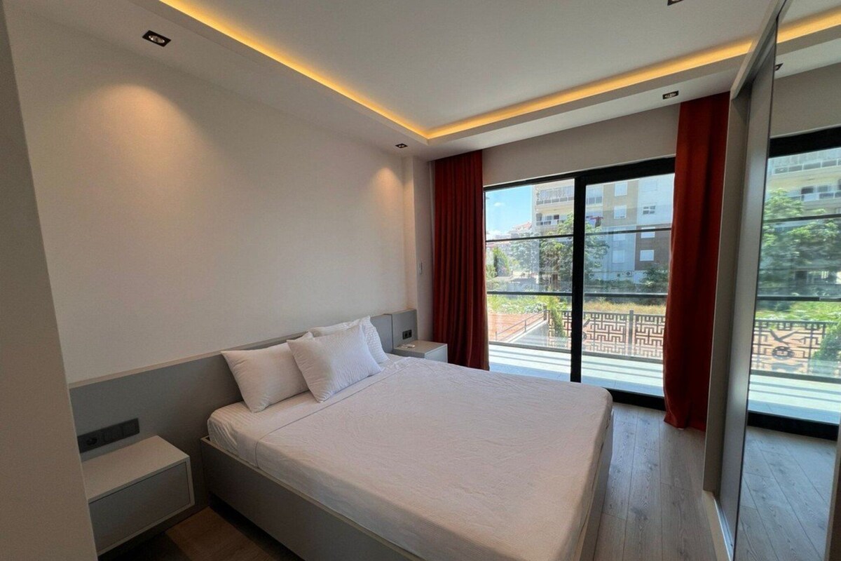 A modern hotel room with a large bed, a nightstand, and a view of a courtyard through a sliding glass door.