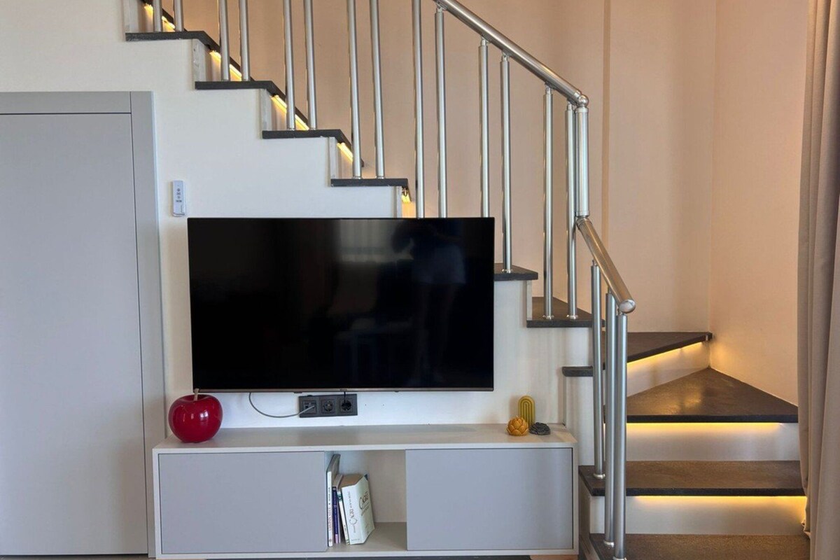 Een moderne trap met een vlak ontwerp, een flatscreen televisie bevestigd aan een witte console, en een rode appel op de console.