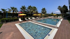 Piscina con múltiples carriles, rodeada de sillas de descanso y sombrillas amarillas.