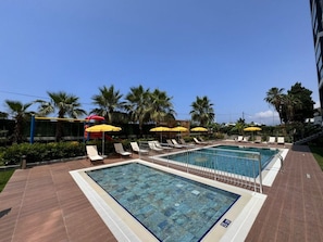 En pool med flera banor, omgiven av solstolar och gula parasoller.