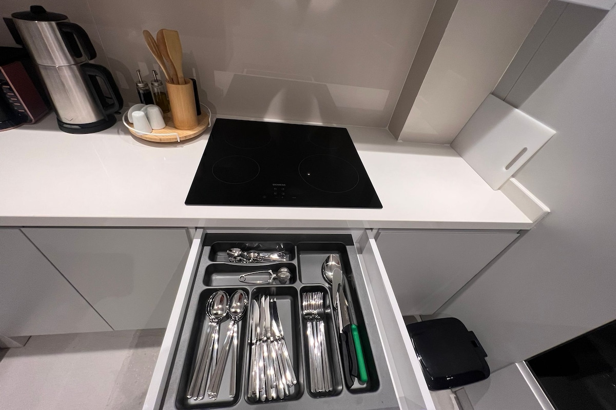 A kitchen with a built-in stove, a coffee maker, and utensils in a drawer.